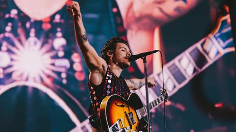 Popstar Harry Styles steht mit Gitarre und ausgebreiteten Armen auf der Bühne bei seinem Stadionkonzert in Frankfurt