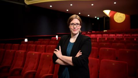 Heleen Gerritse steht mit verschränkten Armen in einem Kinosaal. Hinter ihr sind Reihen roter Kinosessel zu sehen.