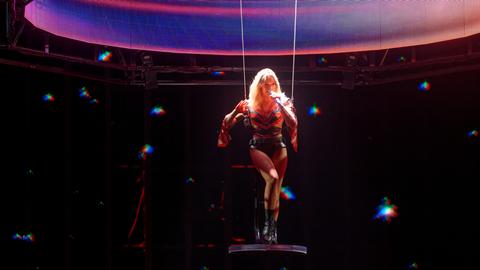 Blone Frau mit Mikrofon schaukelt auf einem Trapez