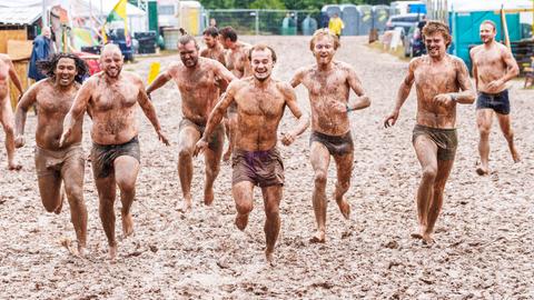 Herzberg-Festival: Sechs Menschen rennen nur mit kurzen Hosen bekleidet durch den Schlamm.