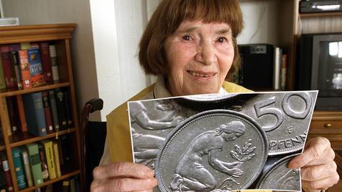 Eine ältere Dame hält ein Foto des 50-Pfennig-Stücks hoch.