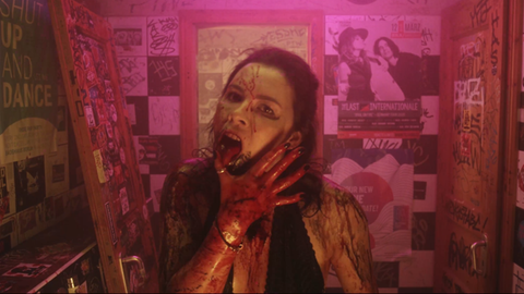 Filmszene aus einer Horror-Comedy-Serie - eine Frau mit Blut im Gesicht leckt sich eine blutige Hand