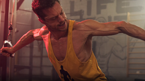 Filmszene einer geplanten Horror-Fitness-Studio-Serie. Ein Mann mit gelbem Achselshirt trainiert mit an einem Gerät im Fitnesstudio.