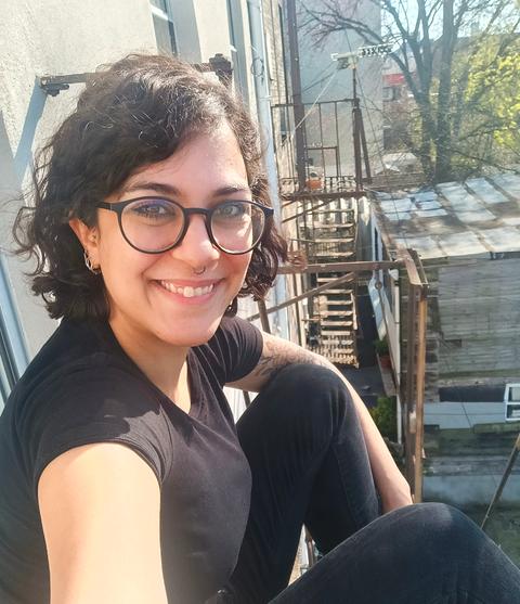 Eine Frau im schwarzem T-Shirt sitzt auf einem Balkon.