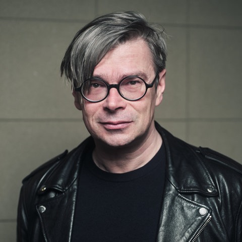 Das Bild zeigt den tschechischen Autoren Jaroslav Rudis. Er trägt seine grauen Haare in einem Seitenscheitel, außerdem eine schwarz gerahmte runde Brille und eine schwarze Lederjacke.