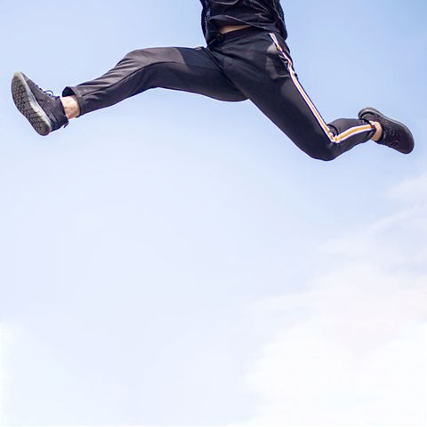 Ein Mann mit Jogginghose springt - vor blauem Himmel aus der Froschperspektive fotografiert.
