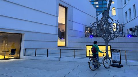 Eine Frau mit Fahrrad steht vor einem blau beleuchteten Kunstwerk