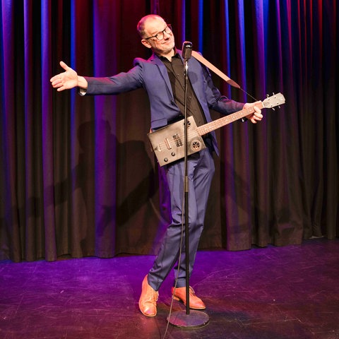 Kabarettist Severin Groebner mit Gitarre auf der Bühne