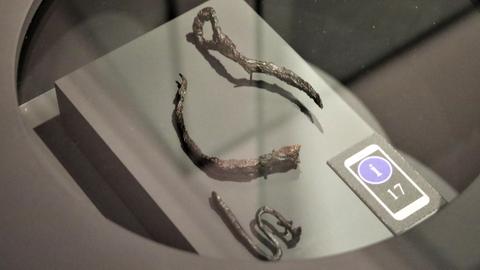 Kleine Eisenstücke, die als Fußfesseln identifiziert sind, in einer Ausstellungsvitrine.
