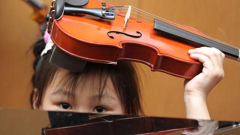 Ein fünfjähriges Kind hält sich eine Geige über Kopf.
