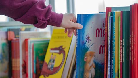 Eine Kinderhand greift nach nach einem Buch aus einem Stapel Bücher