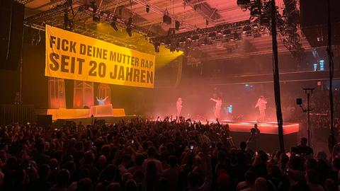 Über der Bühne in der Nordhessen-Arena ist ein großes Banner zu sehen. Darauf steht "Fick Deine Mutter Rap seit 20 Jahren".
