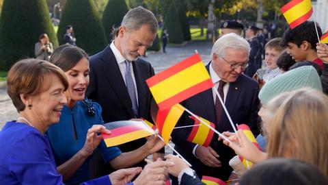 Das spanische Königspaar mit Bundespräsident Frank Walter Steinmeier und dessen Frau Elke Buedenbender in Berlin. Menschen winken mit spanischen und deutschen Fähnchen. 