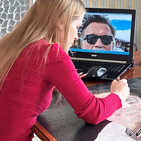 Frau sitzt an einem Tisch vor einem Laptop und zeichnet ein Foto ab.