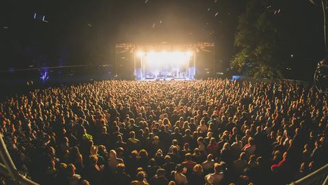 Das Bild ist eine Nachtaufnahme des Sound of the Forest Festivals 2019 und zeigt eine beleuchtete Bühne sowie eine Menschenmenge davor.