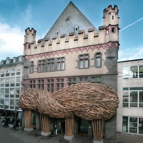 An der Fassade eines Hauses hängt eine baumförmige Skulptur aus Bambus