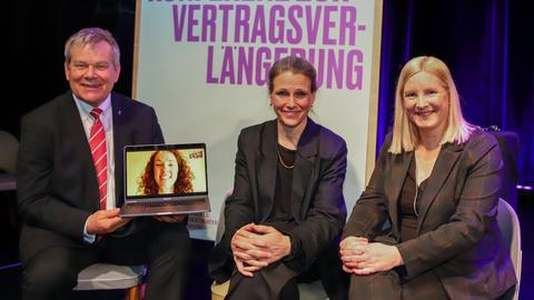 Zwie Frauen und ein Mann, er hält ein Laptop mit dem Bild einer weiteren frau.