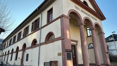 Ein historisch aussehendes Gebäude, das sandfarben gestrichen ist und rot-rosa Säulen hat.
