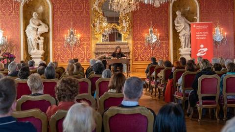Besucher sitzen auf Stühlen in einem Saal des Fuldaer Stadtschloss und hören einer Lesung einer Autorin zu. 