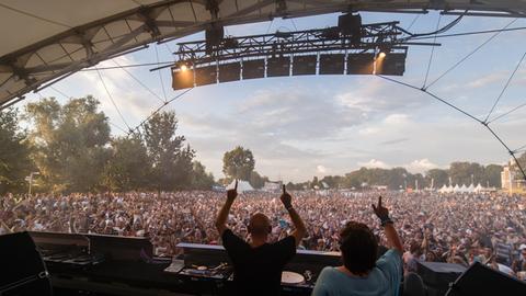 Das Bild zeigt eine Menschenmenge beim Elektro-Festival Love Family Park. Im Bild-Vordergrund sind ein Mann und eine Frau an einem DJ-Pult von hinten zu sehen.