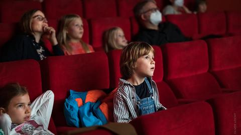 Kinder sitzen auf roten Kinosesseln