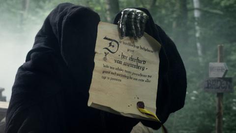 Eine düstere Gestalt in dunklem Kapuzenmantel hält mit einer eisernen Klaue eine Urkunde.