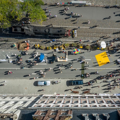 Blick aus der Vogelperspektive auf eine Straße mit Menschen, Fahrrädern und Ständen.