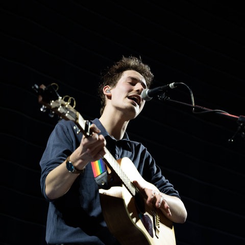 Ein junger Mann steht mit umgehängter Gitarre auf der Bühne.