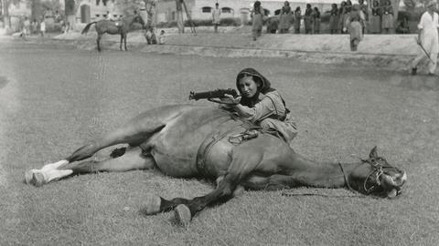 Eine Frau mit Gewehr verschanzt sich in Lahore in Pakistan hinter einem toten Pferd. Aufgenommen wurde das Foto zwischen 1975 und 1958.