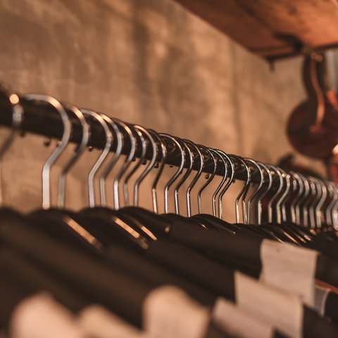 Verschiedene Kleidungsstücke hängen an einer Garderobenstange. 