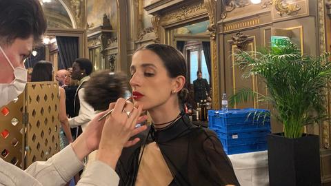 Eine Frau schminkt mit einem Pinsel die Lippen eines dunkelhaarigen Models