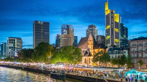 Das Bild zeigt das Museumsuferfest Frankfurt vor der Skyline in der Dämmerung.