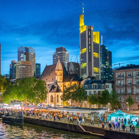 Das Bild zeigt das Museumsuferfest Frankfurt vor der Skyline in der Dämmerung.
