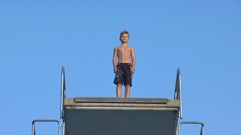 Ein Junge in langer Badeshorts steht auf einem Sprungbrett