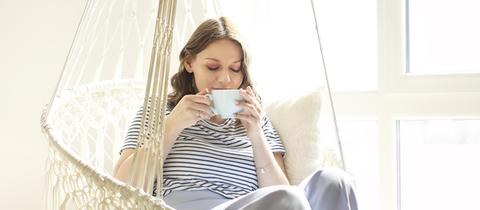 Eine junge Frau genießt in einer Korbschaukel eine Tasse Tee