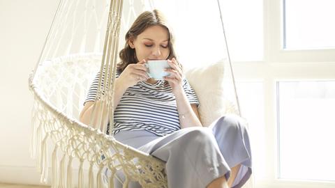 Eine junge Frau genießt in einer Korbschaukel eine Tasse Tee