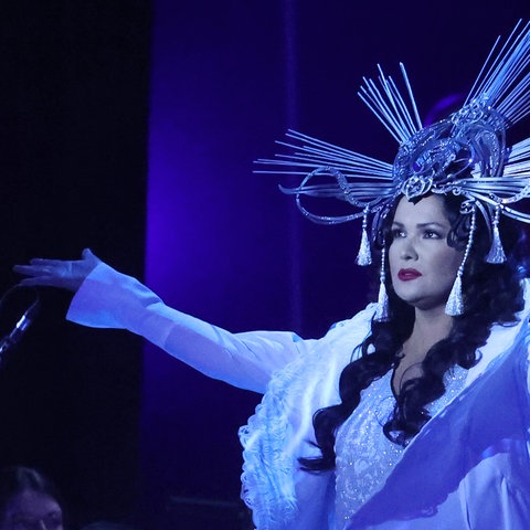 Anna Netrebko mit auffälligem Kopfschmuck im Scheinwerferlicht.