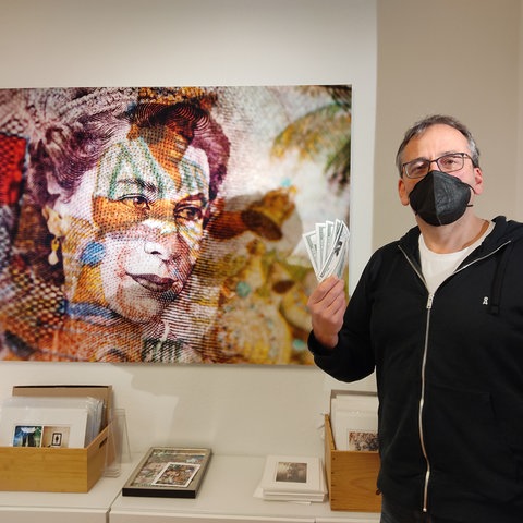 Pete Jones neben einem seiner Werke  - Queen in Geldscheinoptik. Jones hält Geldscheine in der Hand.