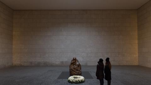 Touristen betrachten in der Gedenkstätte Neue Wache in Berlin die Skulptur "Mutter mit totem Sohn" von Käthe Kollwitz. Davor ist ein Kranz aus weißen Blumen abgelegt.