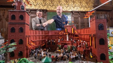 Zwei Männer stehen hinter einer Schloss-Szenerie mit Playmobil-Figuren.