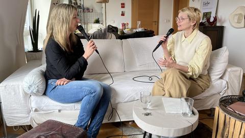 Zwei Frauen sitzen auf einem Sofa, ein Mikrofon in der Hand