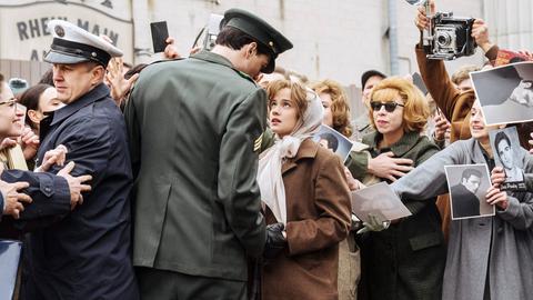 Filmszene aus "Priscilla". Das Bild zeigt Jacob Elordi als Elvis Presley und Cailee Spaeny als Priscilla. Sie stehen in einer Menschenmenge und schauen sich an. Elordi trägt eine grüne Militäruniform, Spaeny einen brauen Mantel und ein Kopftuch.