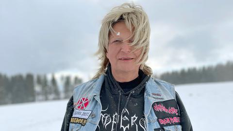 Eine blonde Frau in Rocker-Kluft steht auf einem schneebedeckten Feld.