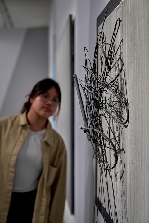 Junge Frau schaut auf ein Metallgeflecht an einer Wand.