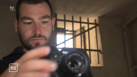 Ein Mann mit Fotoapparat, im Hintergrund ein vergittertes Fenster