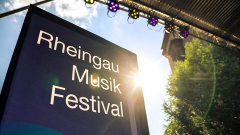 Infotafel mit Aufschrift Rheingau Musik Festival - darüber sind Bühnenscheinwerfer zu sehen