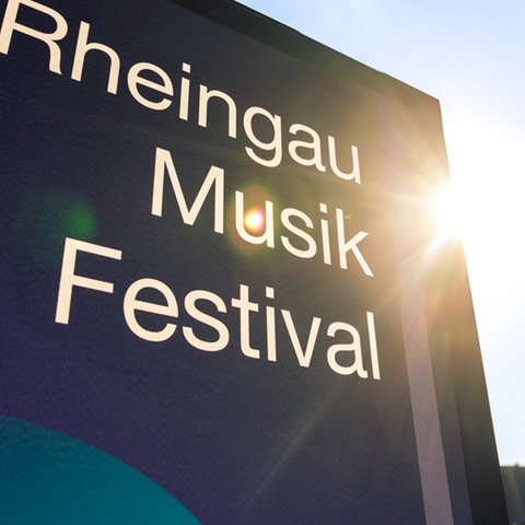 Infotafel mit Aufschrift Rheingau Musik Festival - darüber sind Bühnenscheinwerfer zu sehen