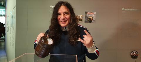 Tankard-Sänger Gerre hält einen Bierkrug mit dem nach der Band benannten Schlagenstern darin in der Hand.