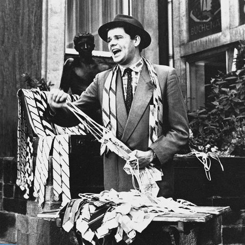 Filmausschnitt aus "Rosen für den Staatsanwalt". Das Schwarz-weiß-Bild zeigt einen Mann mit Hut, der Krawatten verkauft.