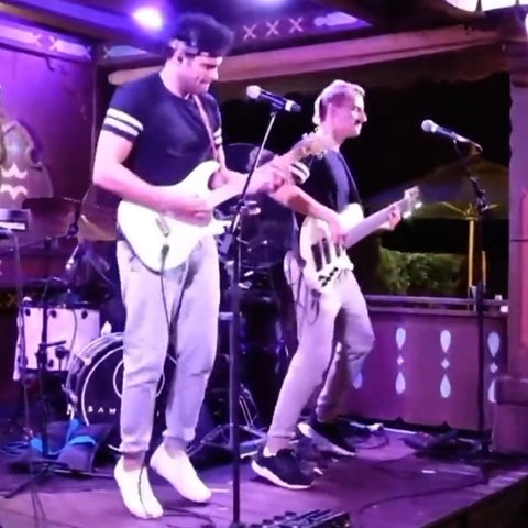 Zwei Musiker mit Gitarre auf einer lila ausgeleuchteten Bühne
